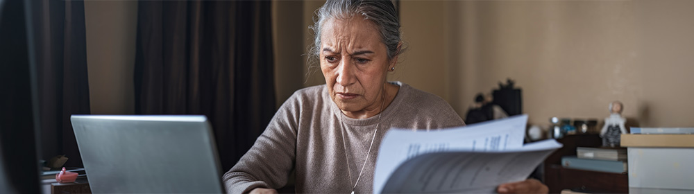 A woman sorts through paperwork at her desk and looks concerned.